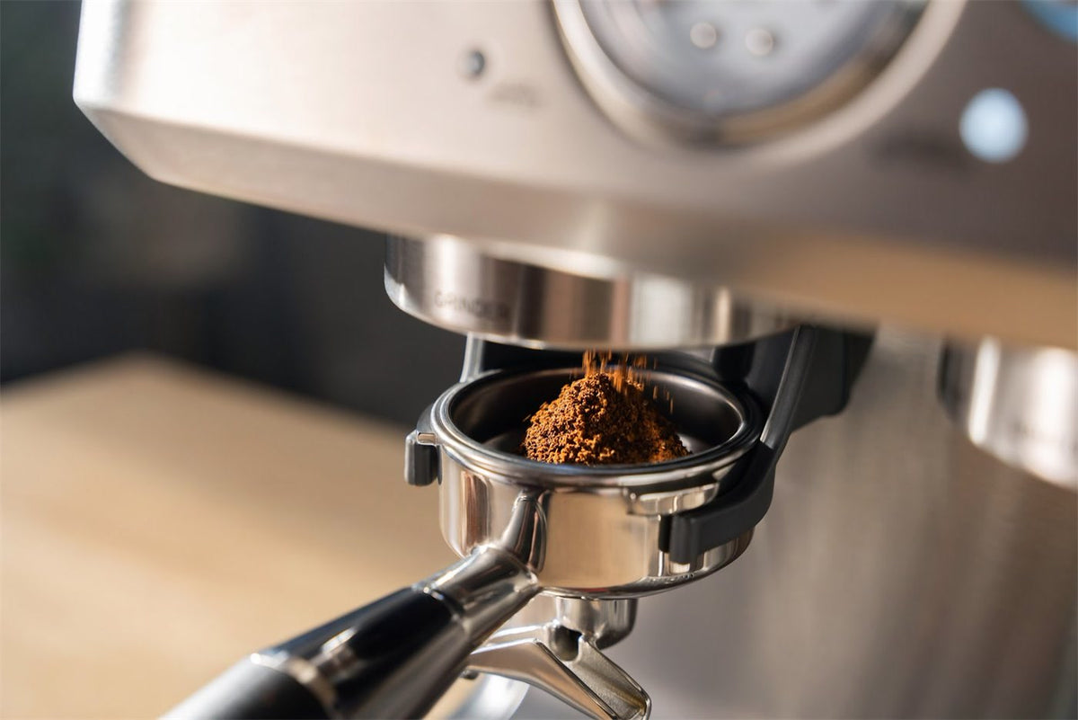 Gemahlener Kaffee rieselt unter dem Mahlwerk einer Espressomaschine aus Edelstahl in einen Siebträger