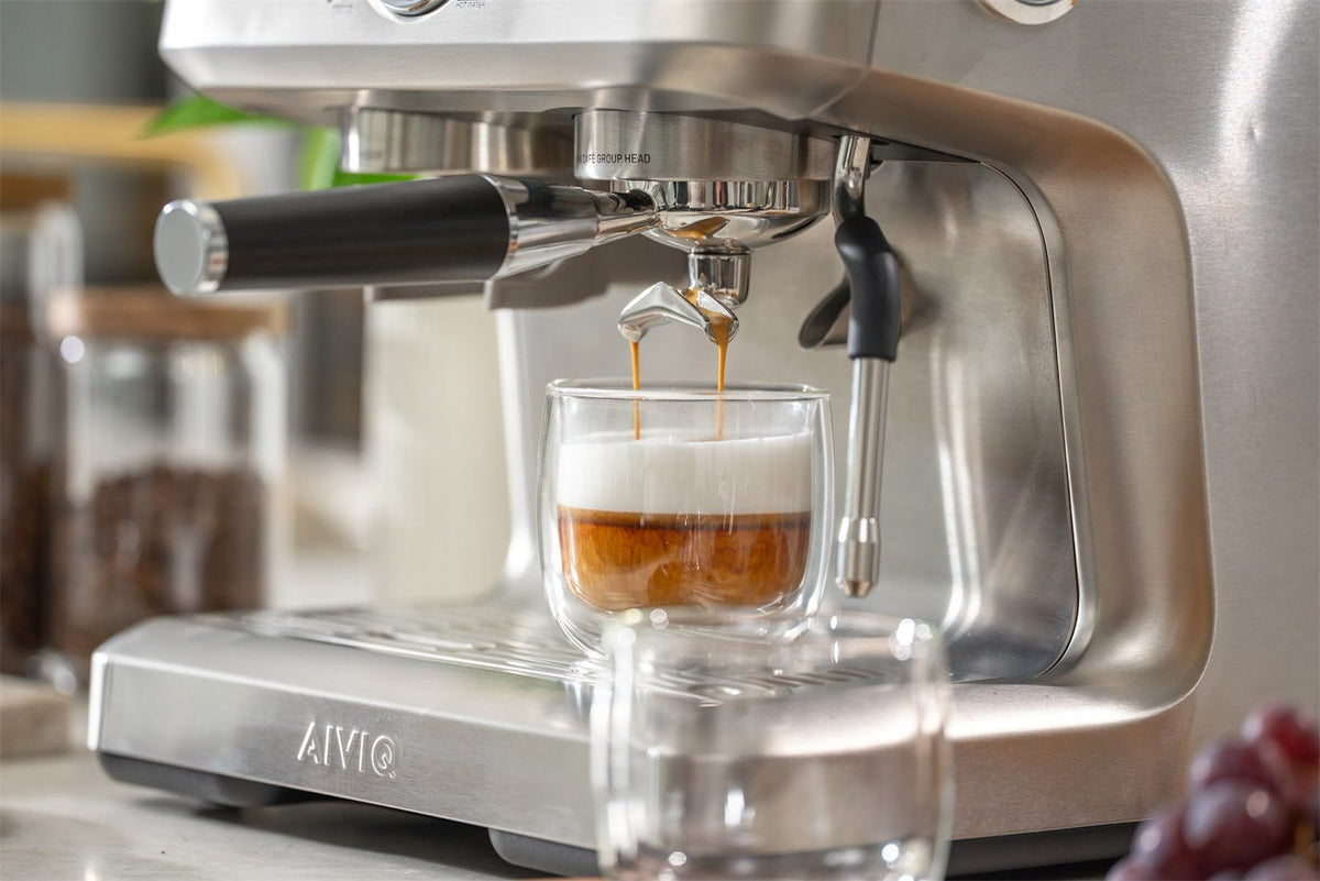 Espresso läuft aus den zwei Ausläufen des Siebträgers in ein Glas mit warmer Milch an einer Espressomaschine aus Edelstahl