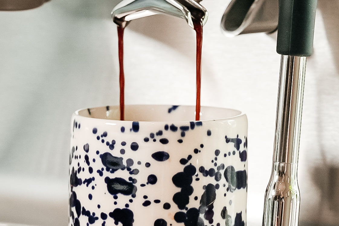 Espresso läuft in zwei dünnen Strahlen aus dem Auslauf des Siebträgers in eine weiße Tasse mit dunkelblauen Punkten an einer AIVIQ Aspire; rechts ist die Dampflanze zu sehen