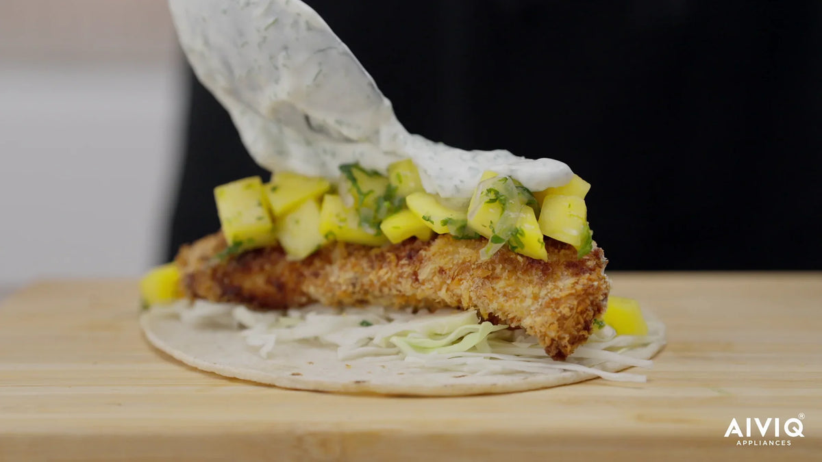 Fish Taco mit paniertem Kabeljau, Mangosalat und Kräutercreme auf einem Schneidebrett