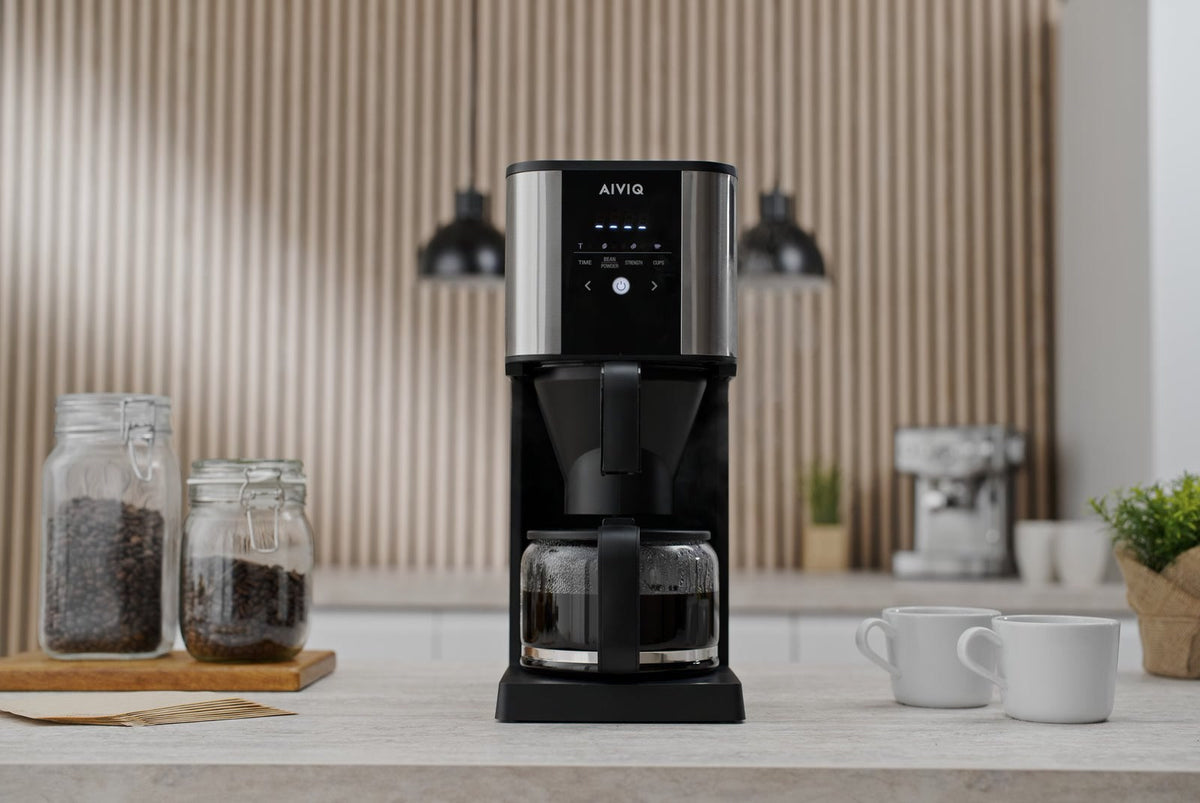 AIVIQ Grind 'N Brew Inspire mit voller Glaskanne auf einer Arbeitsplatte, zwei Gläser mit Kaffeebohnen und zwei weiße Tassen