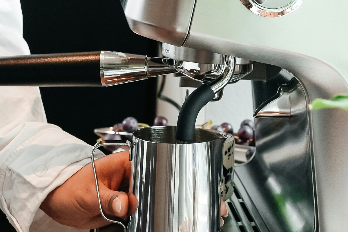 Milch wird mit der Dampflanze in einem Milchkännchen aus Edelstahl an einer AIVIQ Aspire aufgeschäumt