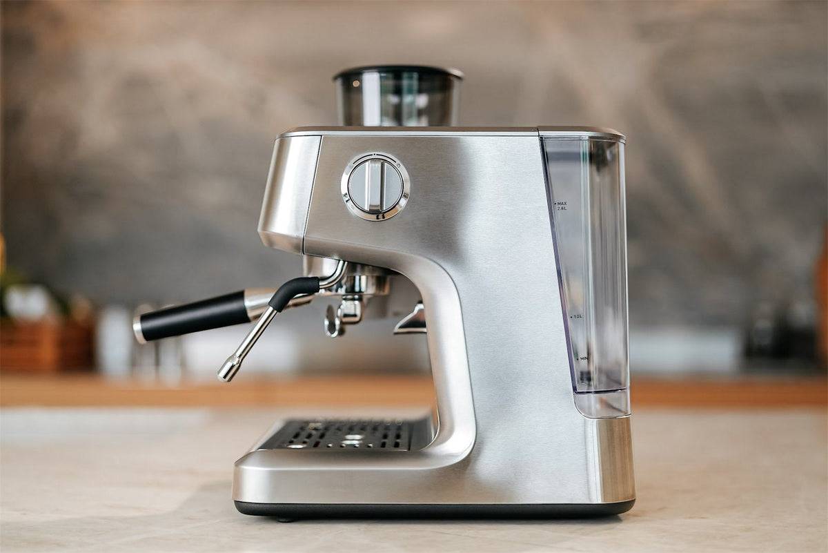Espressomaschine aus Edelstahl von der Seite mit Dampflanze, Siebträger und Wassertank auf einer hellen Arbeitsplatte