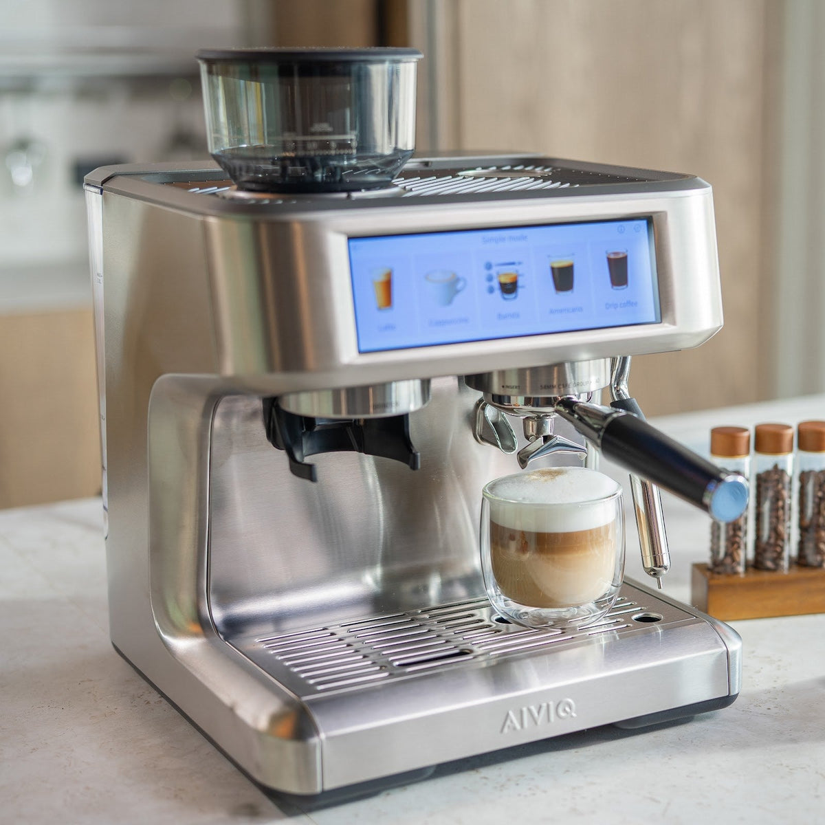 Aspire Expert schräg von links mit einem doppelwandigen Glas mit Kaffee und einer dicken Schicht Milchschaum auf der Abtropfschale. Der Bildschirm steht im Simple mode.